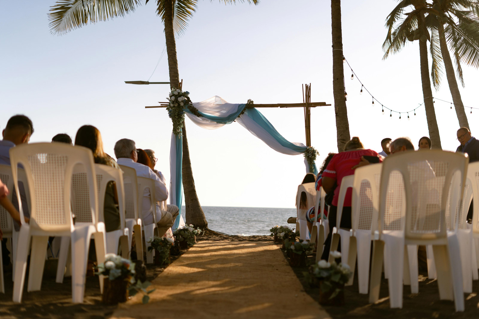 Beachfront wedding ceremony in Cyprus with guests seated on white chairs by the sea.