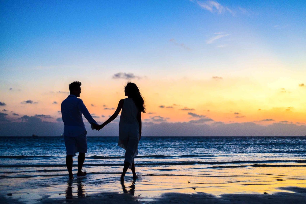 Man and woman on their honeymoon. They are holding hands walking along the beach at sunset.