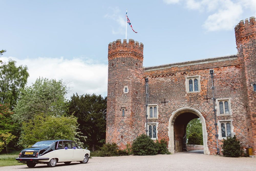 Wedding car parked outside the arched entrance to a castle.